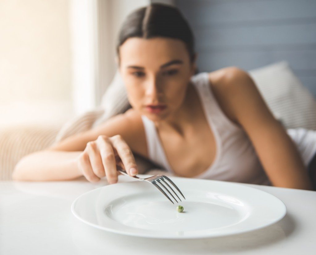 girl eating a single pea using fork