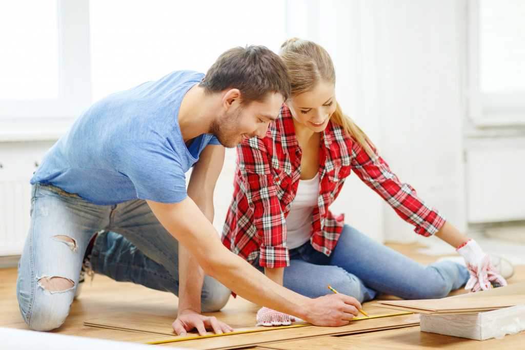 couple measuring floorboard's size in their home