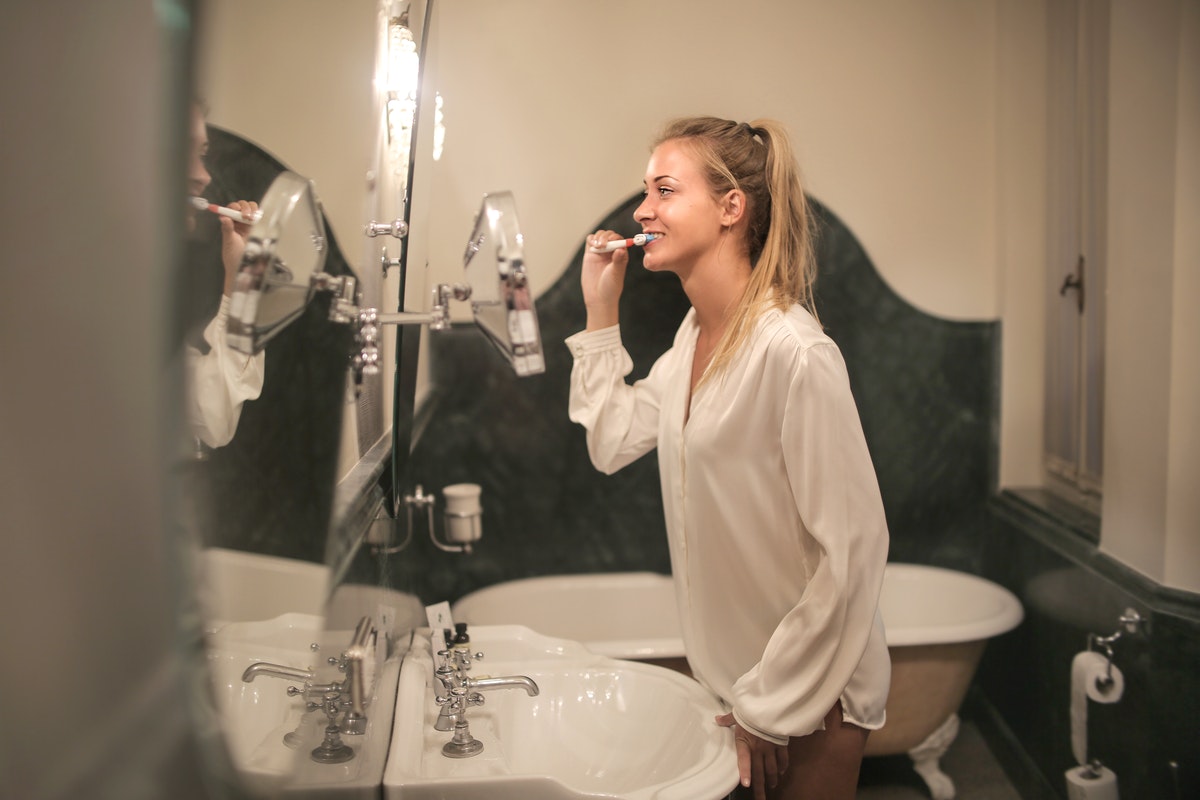 woman brushing her teeth while looking at the mirror