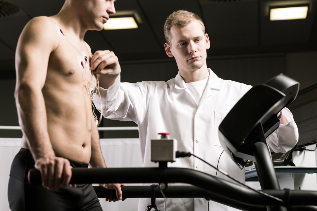 A doctor checking the heart rate of a shirtless man on a treadmill