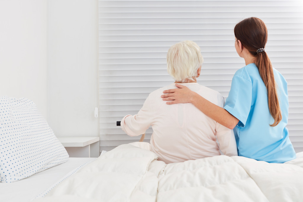 Caregiver sitting next to an elderly woman in bed.