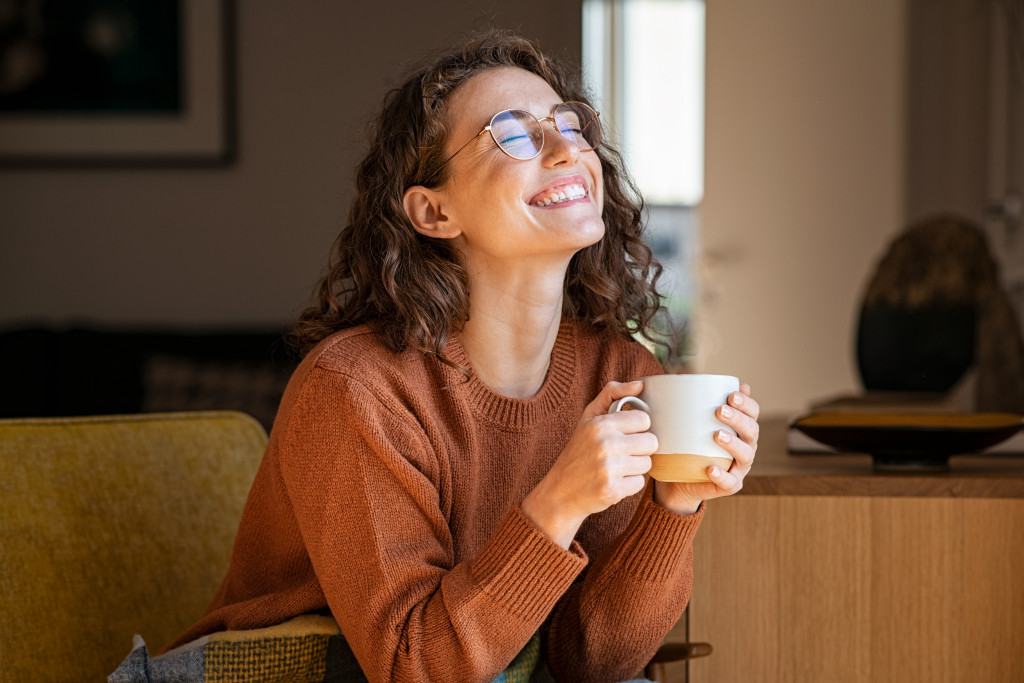 Young woman holding a cup of coffee while sitting on a coach at home.